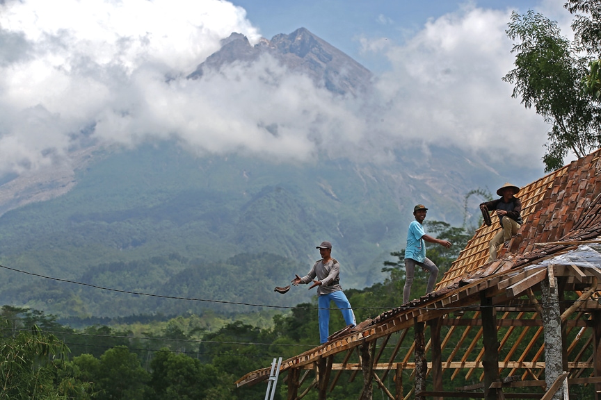 TETAP BERAKTIVITAS: Warga membetulkan atap rumah di lereng Gunung Merapi, Cangkringan, Sleman, kemarin (19/11). (HENDRA EKA/JAWA POS) - Image