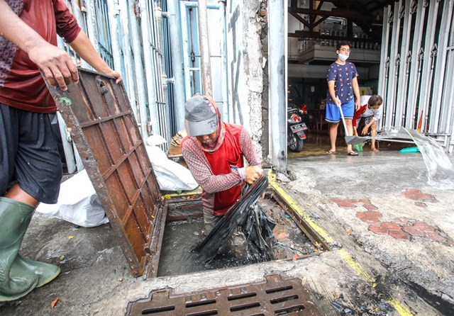 GERAK CEPAT: Petugas membongkat saluran yang tersumbat. Tumpukan sampah lantas diangkut agar aliran air kembali lancar. (Dipta Wahyu/Jawa Pos) - Image