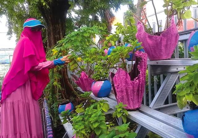 WARNA-WARNI: Ketua KWT Dorang Cinta Diyah Indra Oktavianti menunjukkan salah satu sudut Taman Dorang Cinta. Tampak handuk bekas yang diolah jadi pot tanaman. (Ahmad Khusaini/Jawa Pos) - Image