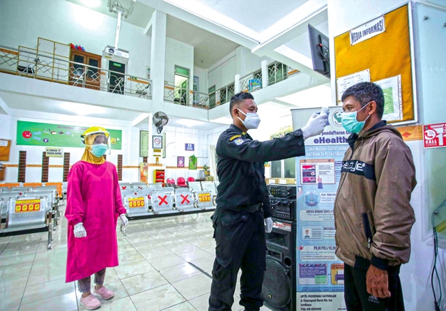 SIAGA 24 JAM: Petugas linmas didampingi dokter Ike Nur Alinda sedang mengecek suhu warga sebelum masuk dan menjalani pemeriksaan di dalam Puskesmas Gayungan, Selasa (13/7). Puskesmas di Kota Surabaya beroperasi 24 jam hingga 20 Juli. (Alfian Rizal/Jawa Po - Image