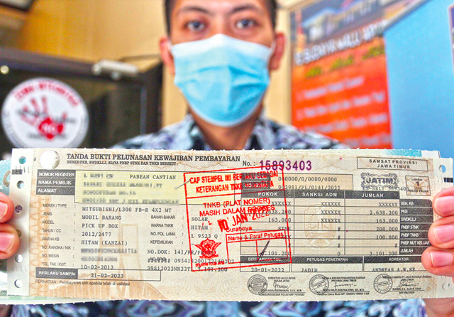 PENGGANTI PELAT: Pamin Samsat Surabaya Utara Iptu Muhammad Romaji menunjukkan stempel pada STNK kendaraan roda empat yang menerangkan TNKB (pelat nomor) masih dalam proses akibat material belum tersedia (20/1). (Ahmad Khusaini/Jawa Pos) - Image
