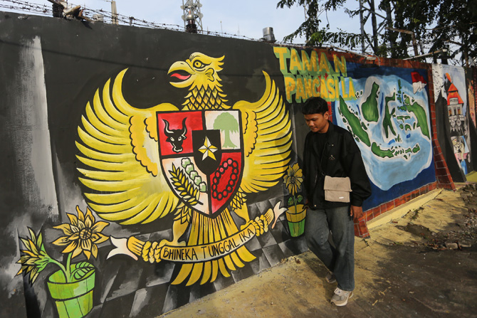 Warga melintas di depan mural lambang pancasila dan peta Indonesia di kawasan Beji, Depok, Jawa Barat, Senin (4/7/2022). Mural tersebut sebagai media edukasi kepada masyarakat agar selalu menjaga toleransi dan persatuan bangsa meskipun berbeda suku dan a - Image