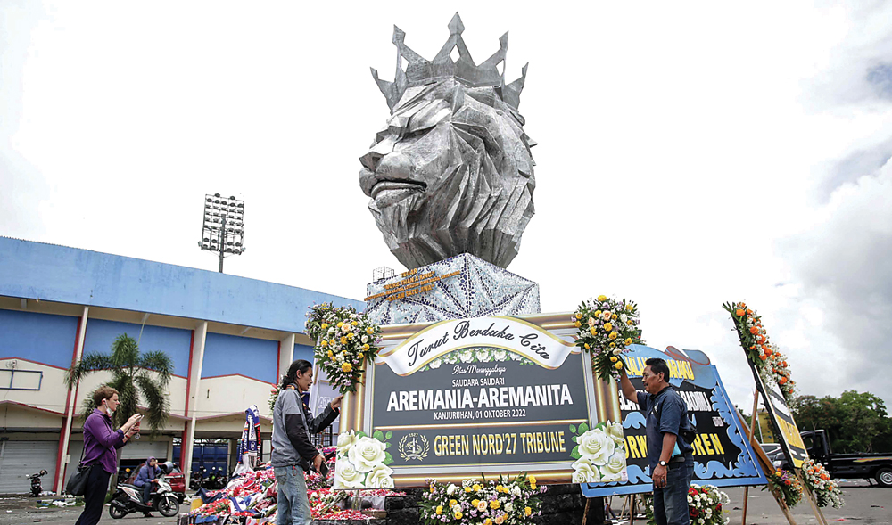 DARI SURABAYA UNTUK MALANG: Pekerja mengantar karangan bunga berisi ucapan belasungkawa dari suporter Persebaya untuk Aremania dan Aremanita di Stadion Kanjuruhan, Kabupaten Malang, kemarin (3/10). (ALFIAN RIZAL/JAWA POS) - Image