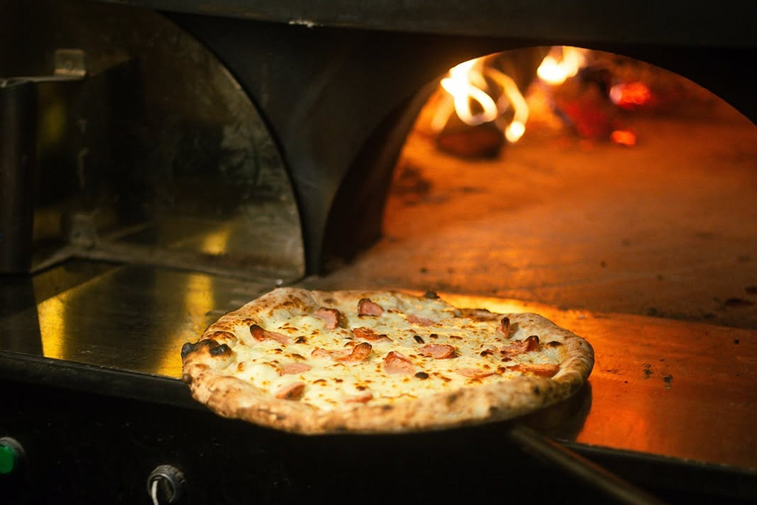 Pizza yang dimasak menggunakan oven tungku kayu.