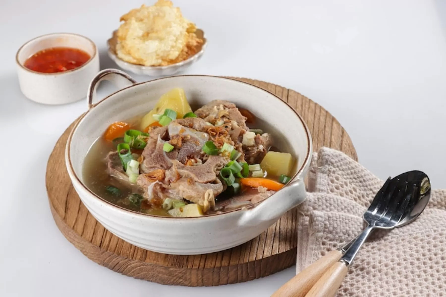 Ilustrasi sajian sop buntut sapi lengkap dengan emping dan sambal yang siap disantap. (Dok. Freepik)