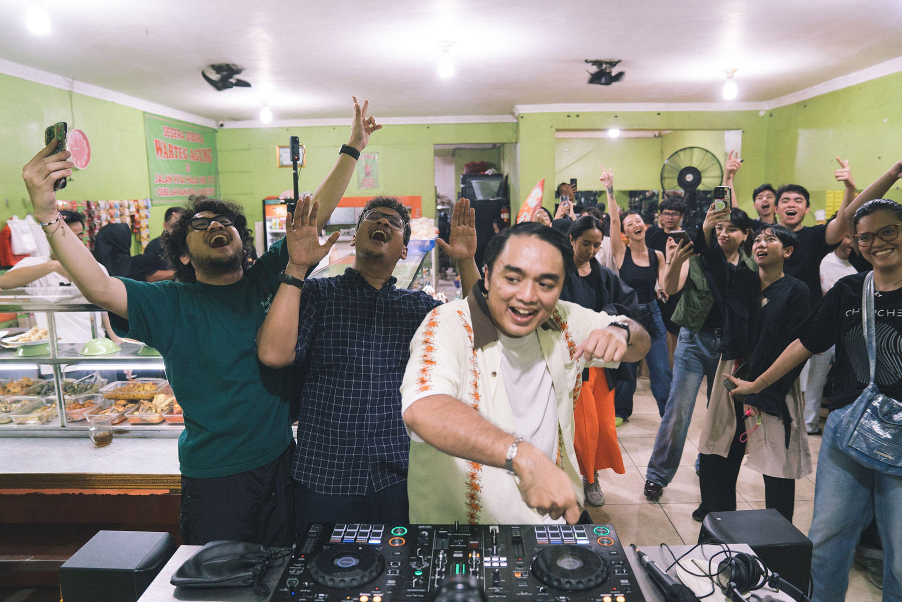 Dipha Barus beraksi memainkan Rima Raga dan beberapa lagu hit yang diedit sedemikian rupa menjadi soundtrack pesta rilis rahasia di salah satu warteg.