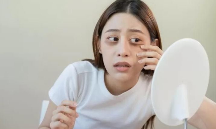 Ilustrasi seorang perempuan yang sedang memerhatikan lingkaran hitam di bawah matanya