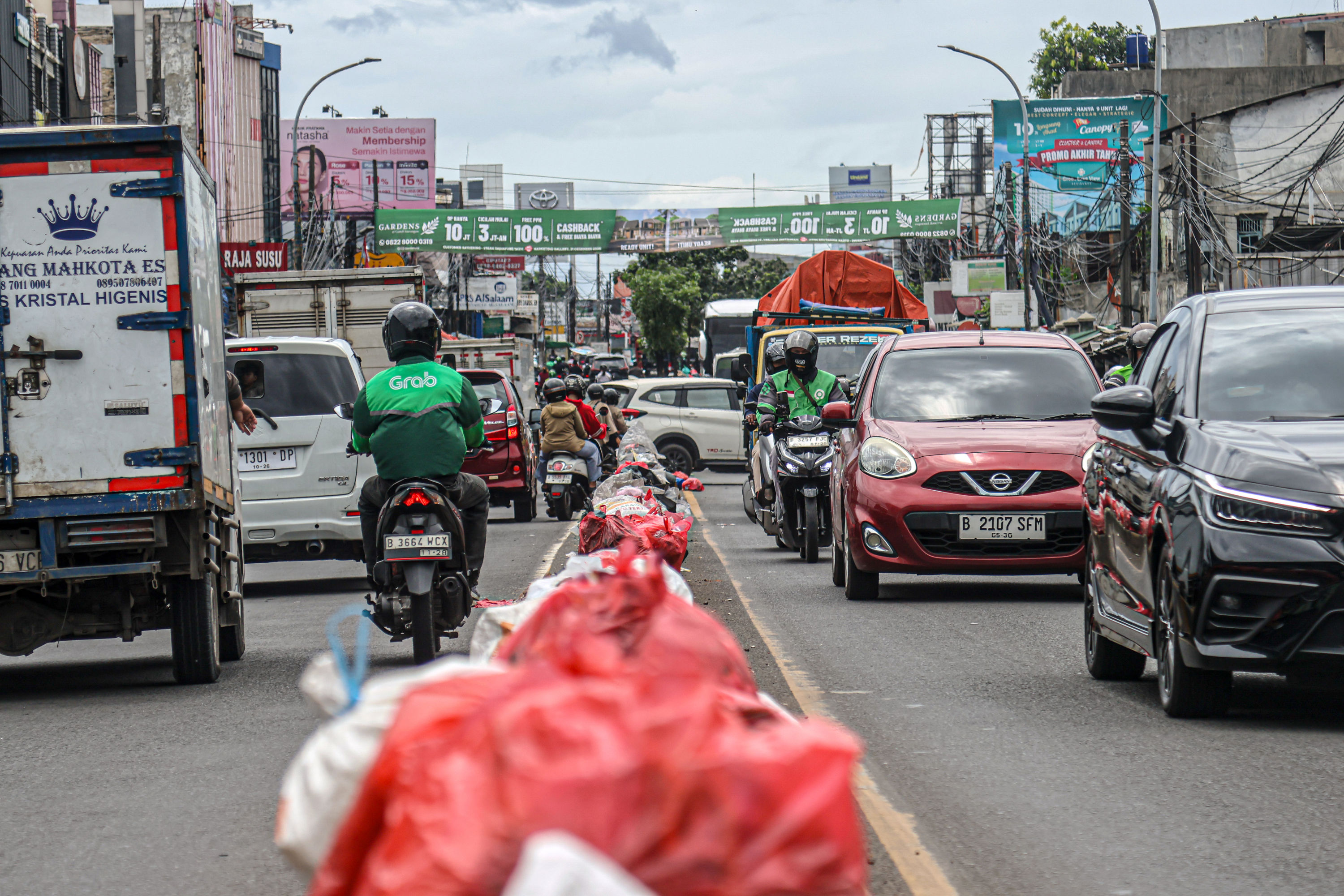 Aktifitas warga di sekitar tumpukan sampah di Jalan Dewi Sartika, Ciputat, Tangerang Selatan, Selasa (16/12/2025). Sampah yang menumpuk di pinggir jalan tersebut disebabkan adanya penataan gunungan sampah di Tempat Pembuangan Akhir (TPA) Cipeucang sehingg