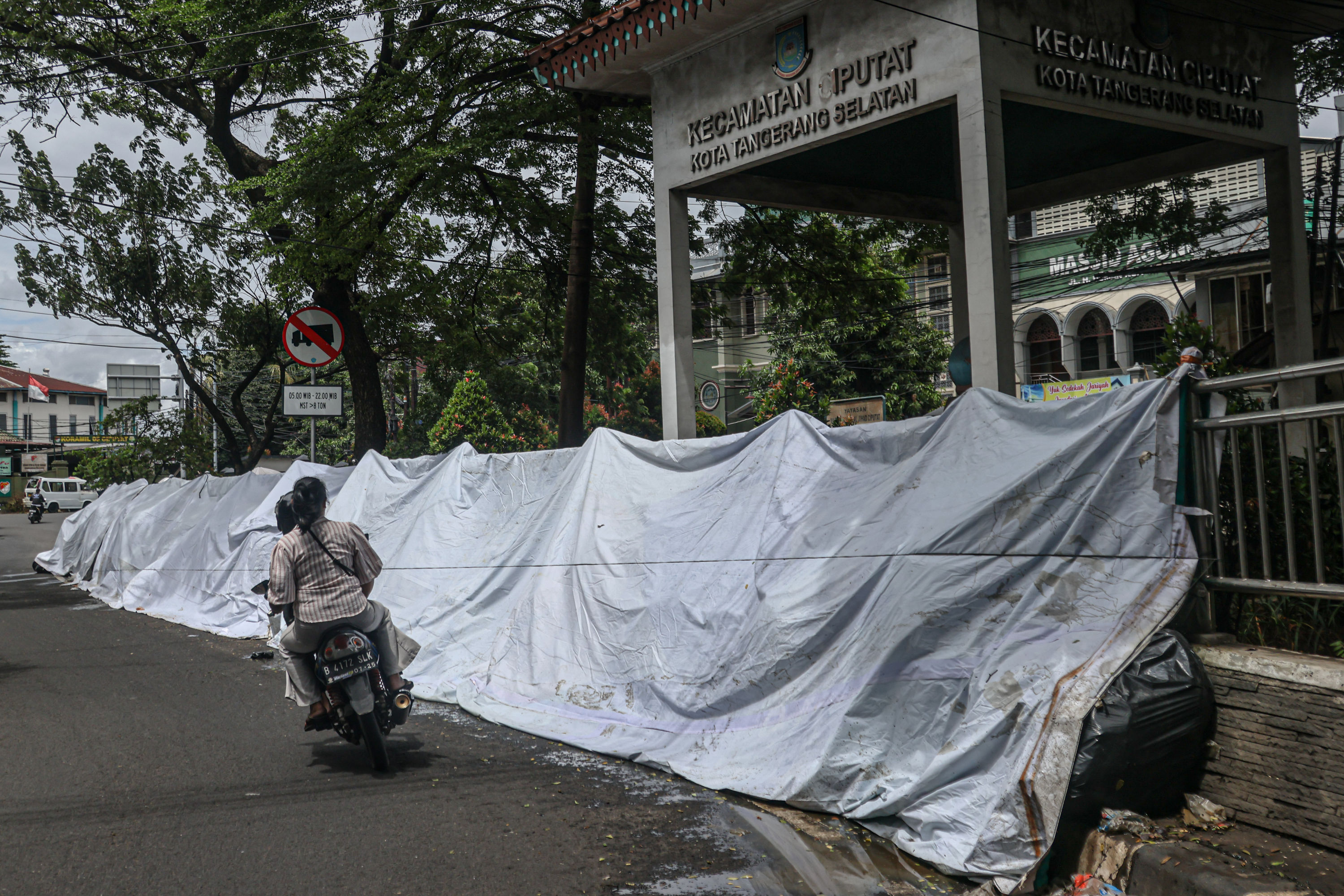 Aktifitas warga di sekitar tumpukan sampah di Jalan Dewi Sartika, Ciputat, Tangerang Selatan, Selasa (16/12/2025). Sampah yang menumpuk di pinggir jalan tersebut disebabkan adanya penataan gunungan sampah di Tempat Pembuangan Akhir (TPA) Cipeucang sehingg