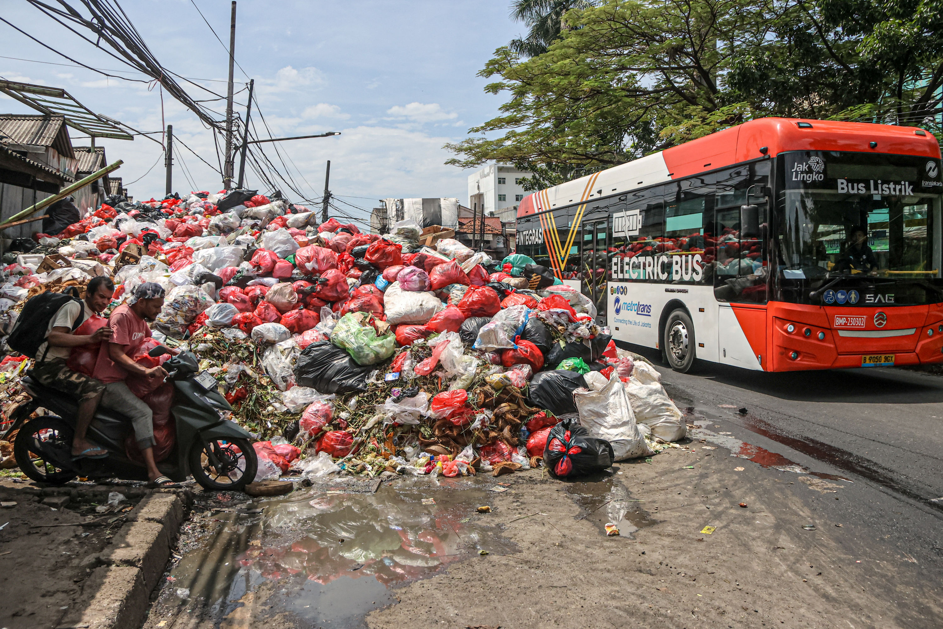 Sejumlah pengendara melintas di tumpukan sampah yang berada di depan pasar Cimanggis, Tangerang Selatan, Selasa (06/01/2025). Tumpukan sampah yang mencapai tiga meter tersebut dikarenakan masih belum optimalnya TPA Cipeucang untuk menampung sampah dari Ta