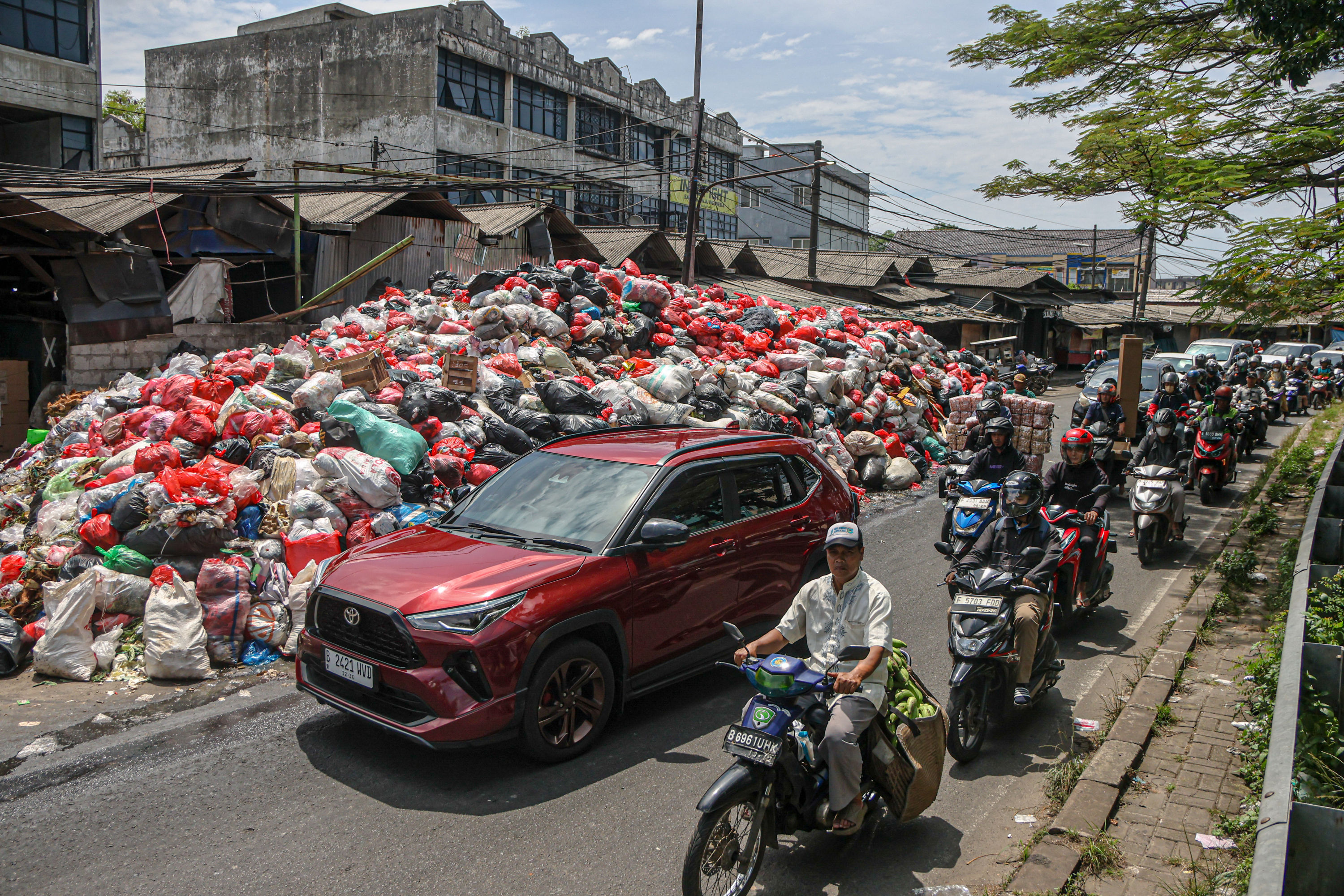 Sejumlah pengendara melintas di tumpukan sampah yang berada di depan pasar Cimanggis, Tangerang Selatan, Selasa (06/01/2025). Tumpukan sampah yang mencapai tiga meter tersebut dikarenakan masih belum optimalnya TPA Cipeucang untuk menampung sampah dari Ta